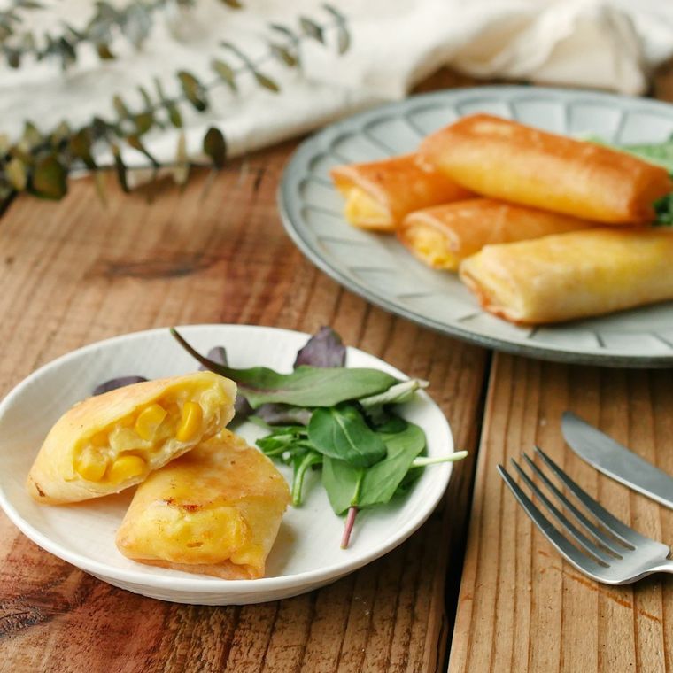 小さな丸の器に半分に切ったコーンクリーム春巻きと野菜がのっている
