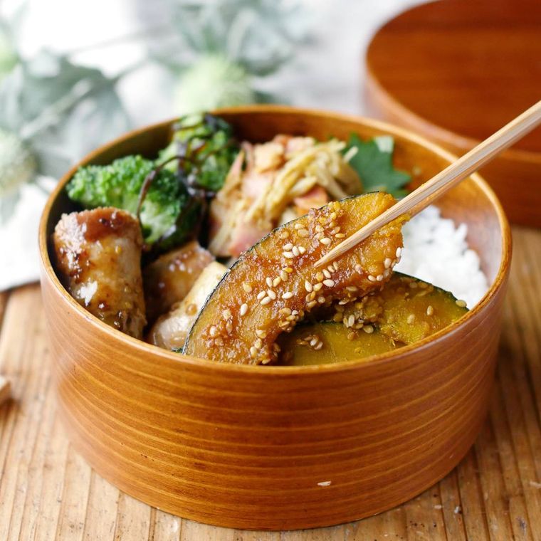 お弁当箱に入ったかぼちゃの甘辛焼きを箸で掴んでいる様子