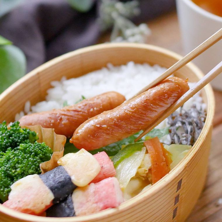 お弁当箱に入っているウインナーを箸で持ち上げているところ