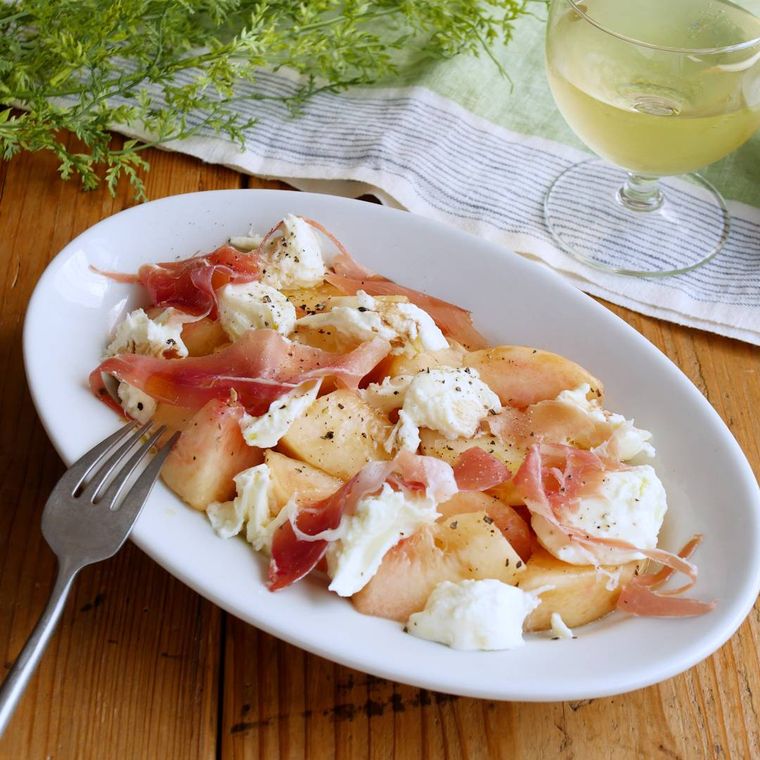 白いオーバル皿に盛られた桃、モッツアレラ、生ハムにバルサミコ酢かけ