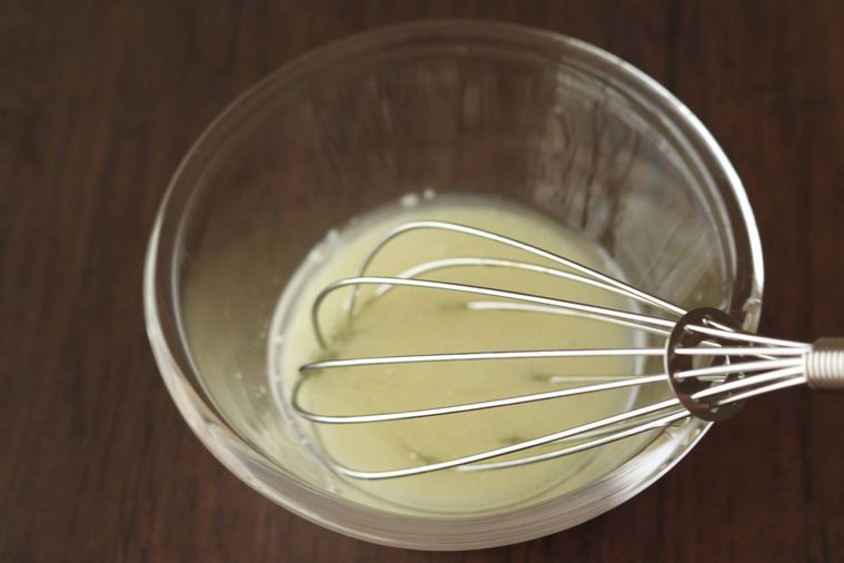 容器に入っている白い液体を泡だて器で混ぜている