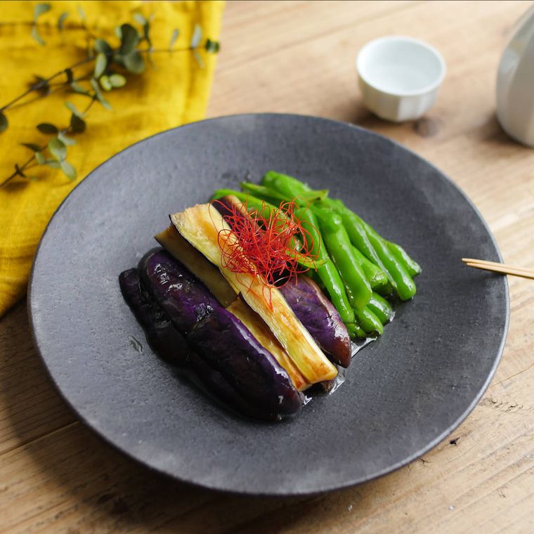 黒い丸皿に盛り付けられたなすとピーマンの中華風焼き浸し
