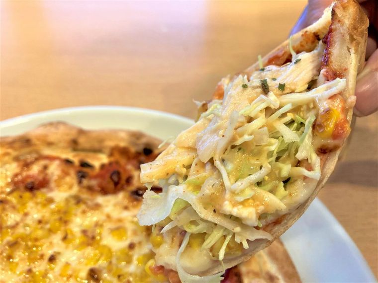 たっぷりマヨコーンピザの上にサラダをのせ、持ち上げている