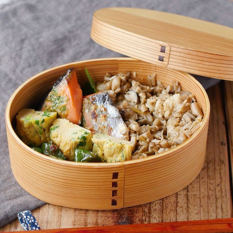 曲げわっぱの弁当箱に入った、きのこの混ぜごはんと鮭の味噌焼き、ねぎ入り卵焼き、ピーマンのおかか和え
