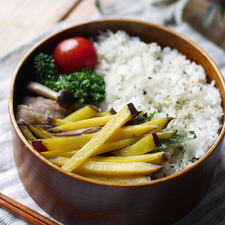 丸い弁当箱に入った、さつまいものソテーとごはん、ミニトマトとパセリ