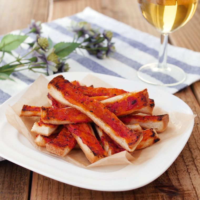 白い皿に盛られた、食パンの耳にすりおろしトマトとにんにくをのせて焼いたもの