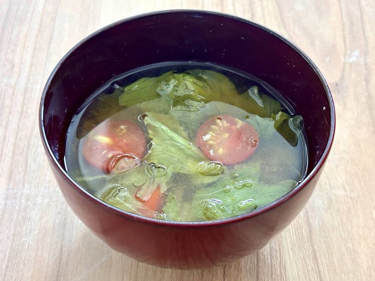 レタスとミニトマトのみそ汁が赤い汁椀に入っているところ