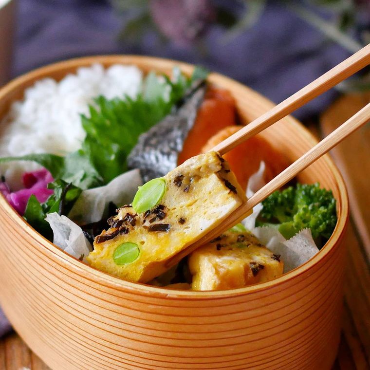 お弁当箱に入ったはんぺんと塩昆布の卵焼きを箸でつまんでいる様子