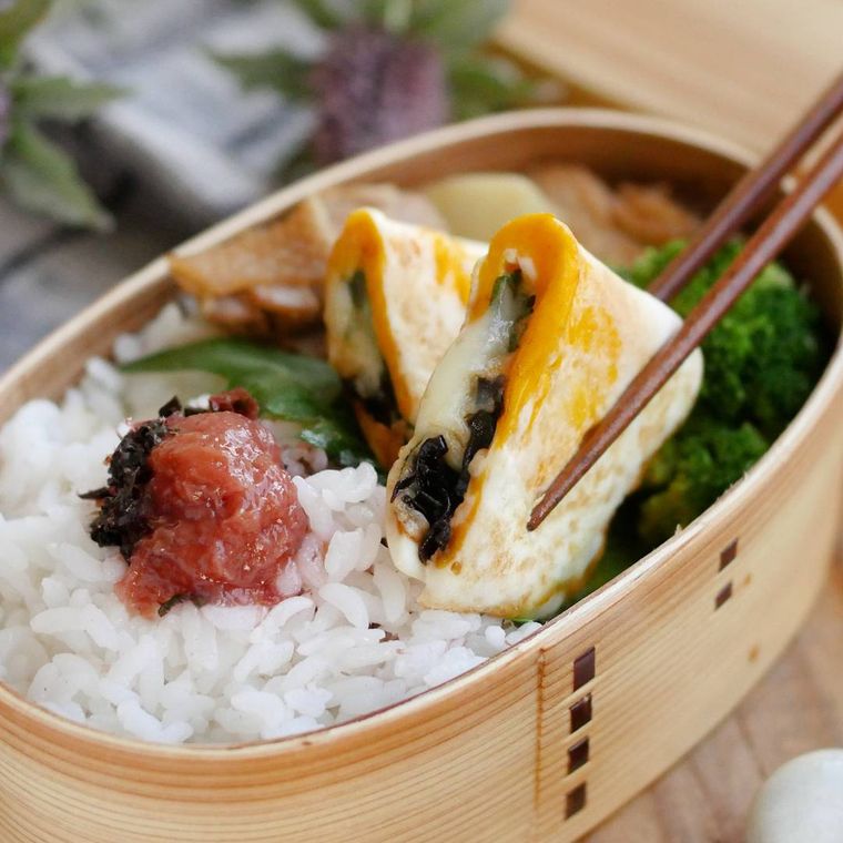 お弁当箱に入った塩こんぶチーズの半月卵を箸でつまんでいる様子