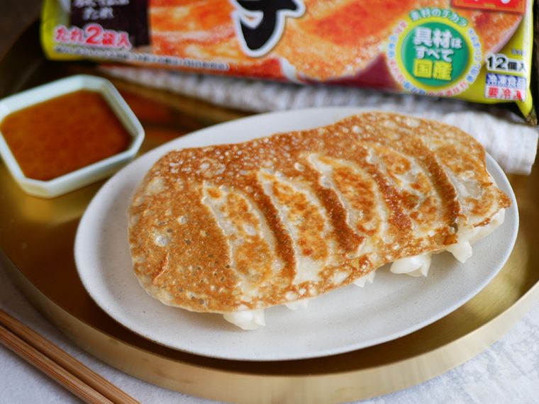 白い皿にのった焼き餃子とタレ、奥に大阪王将羽根つき餃子のパッケージが見えている様子