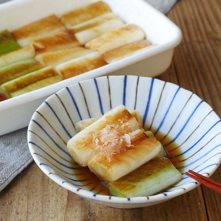 縦縞模様の白い器に盛りつけられた長ねぎのしょうがしょうゆ焼きびたし