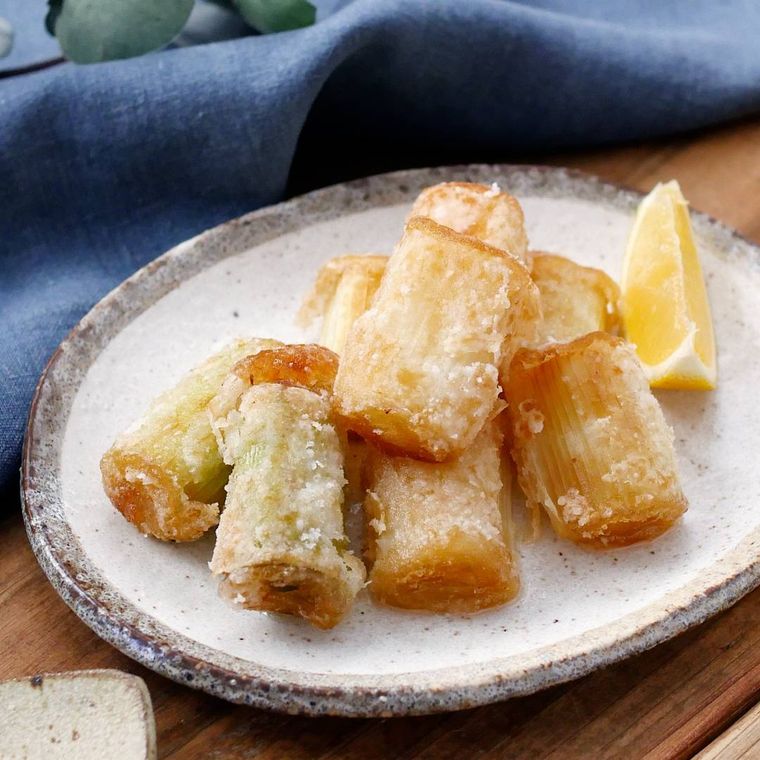 茶色い縁取りの白い皿にレモンとともに盛りつけられた長ねぎの唐揚げ