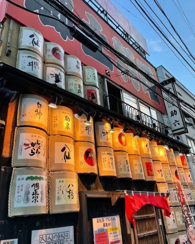 赤い看板がかかり日本酒の樽がディスプレイされた助六 青森駅前アウガ隣店の外観