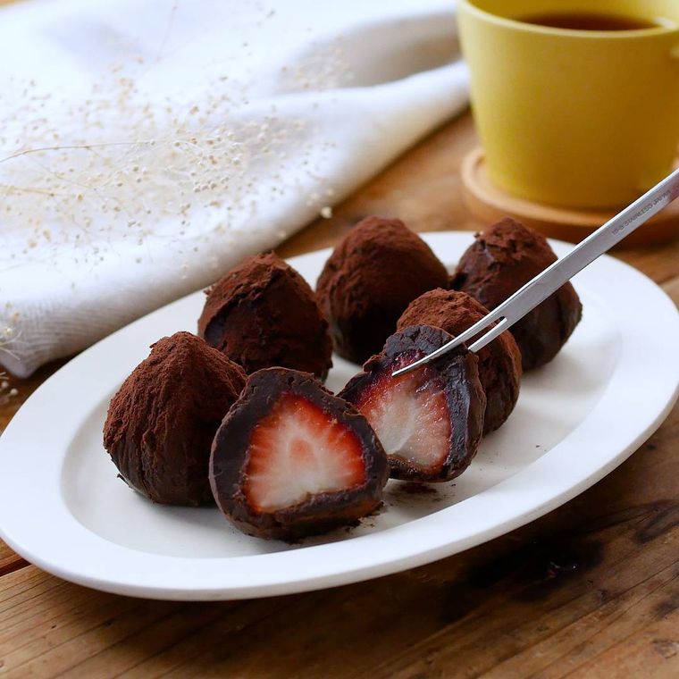 白い皿に並べた生クリームを使ったいちごトリュフをフォークで持ち上げているところ