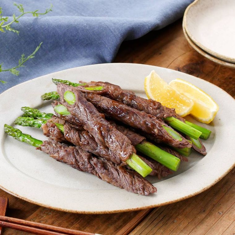 白い丸皿にレモンとともに盛り付けられたアスパラガスの牛肉巻き