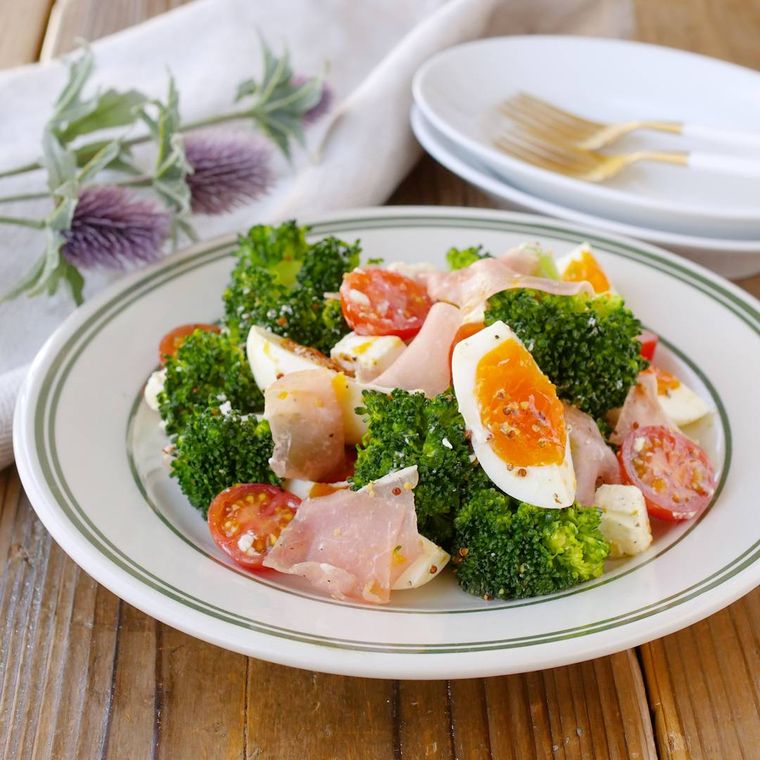 白地に緑のふちの丸皿に盛り付けられたブロッコリーと生ハムのサラダ