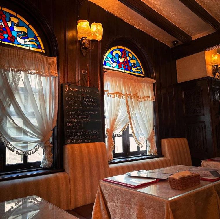 ステンドグラスが壁にありテーブル席が並んだクレープリー・アルションの店内