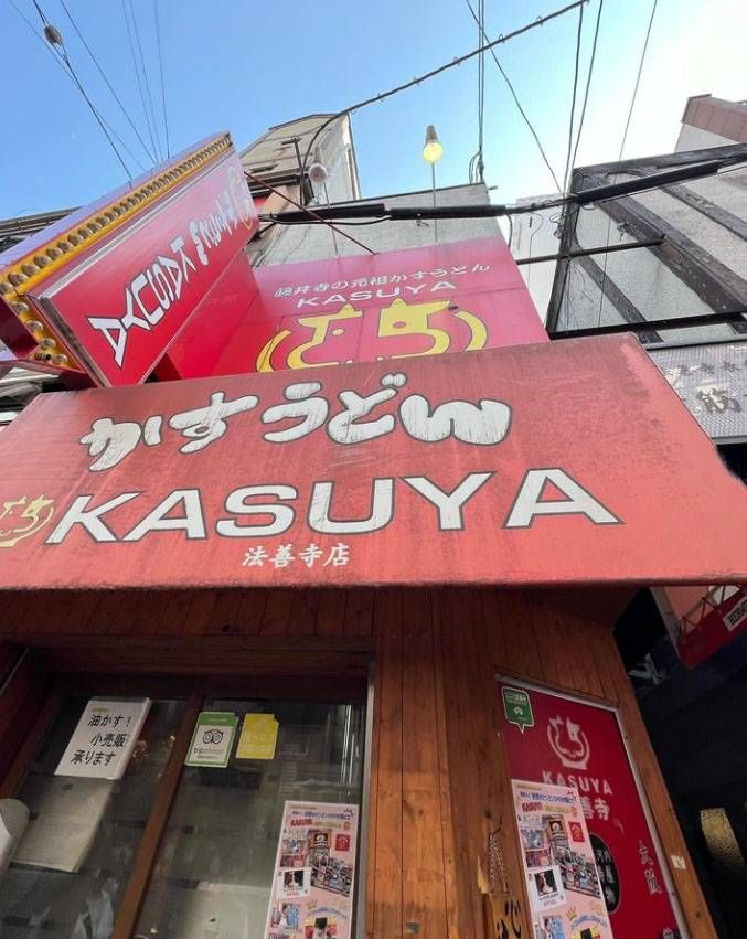 赤い看板に牛のイラストが描かれたカスヤ 法善寺店の外観