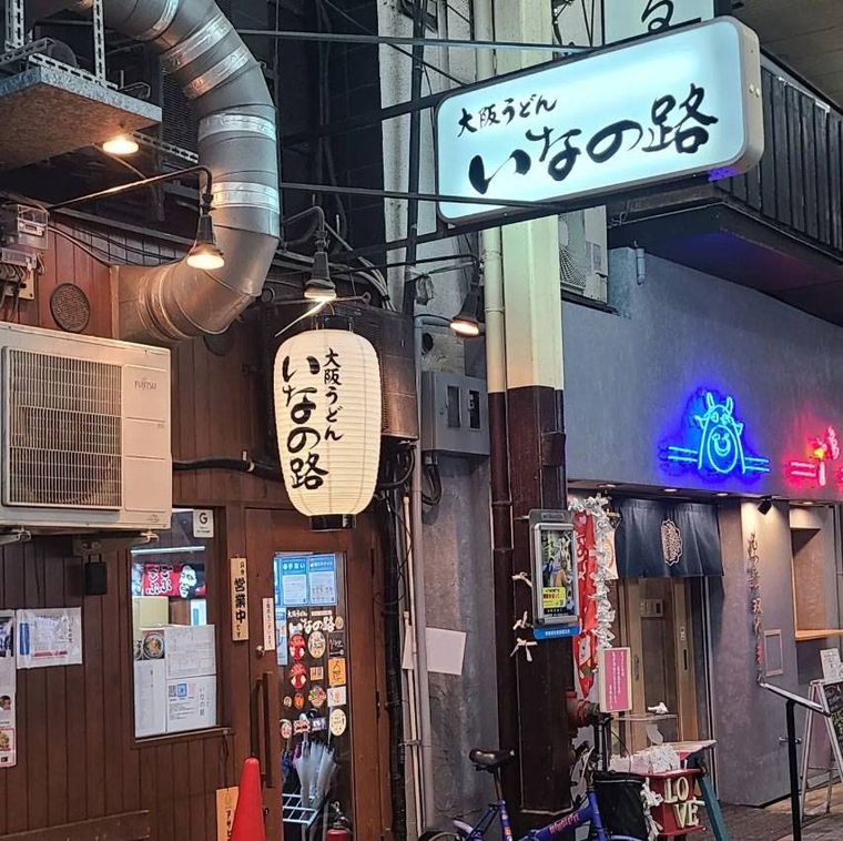 茶色の外壁に白いちょうちんがかかった大阪うどん いなの路の外観