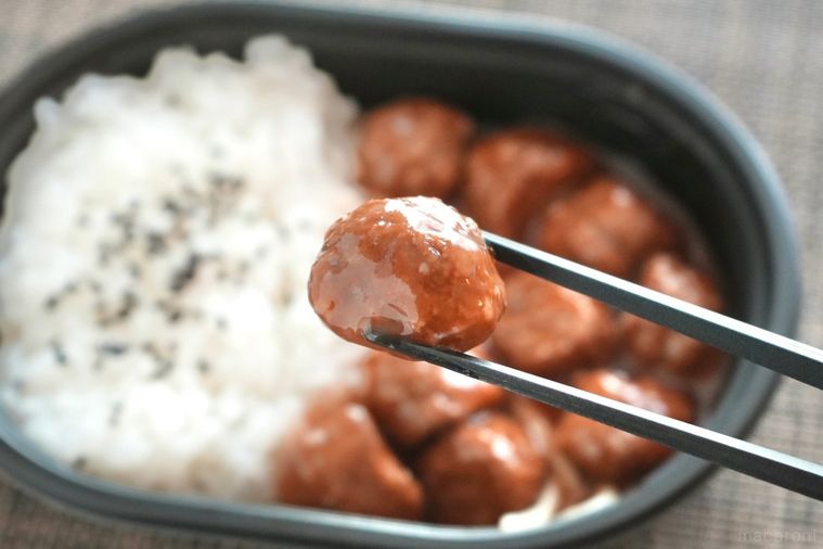 お弁当のミートボールを黒い箸で持ち上げる様子