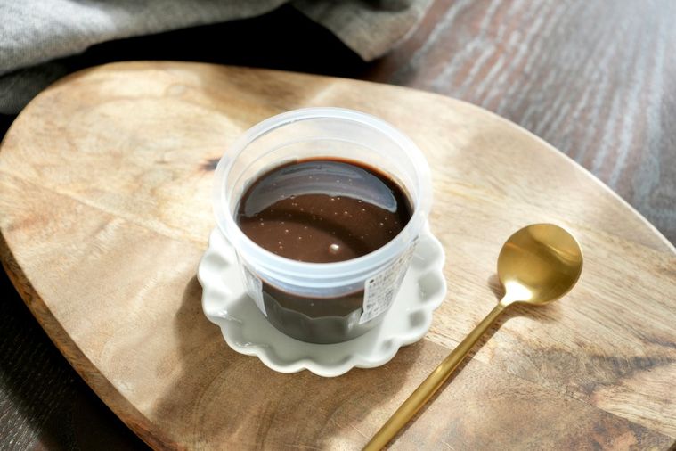 木のカッティングボードと白い小皿にのった黒いショコラプリンと金のスプーン