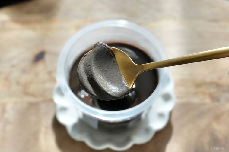 木のカッティングボードと白い小皿にのった黒いショコラプリンを金のスプーンで食べる様子