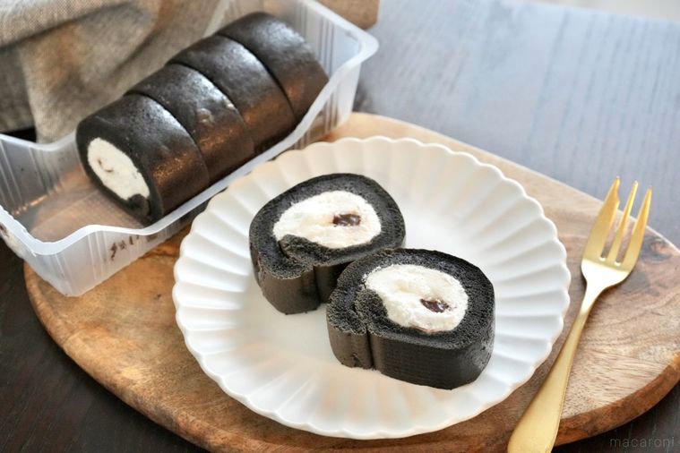 木のカッティングボードと白い皿にのったモノクロのロールケーキと金のフォーク