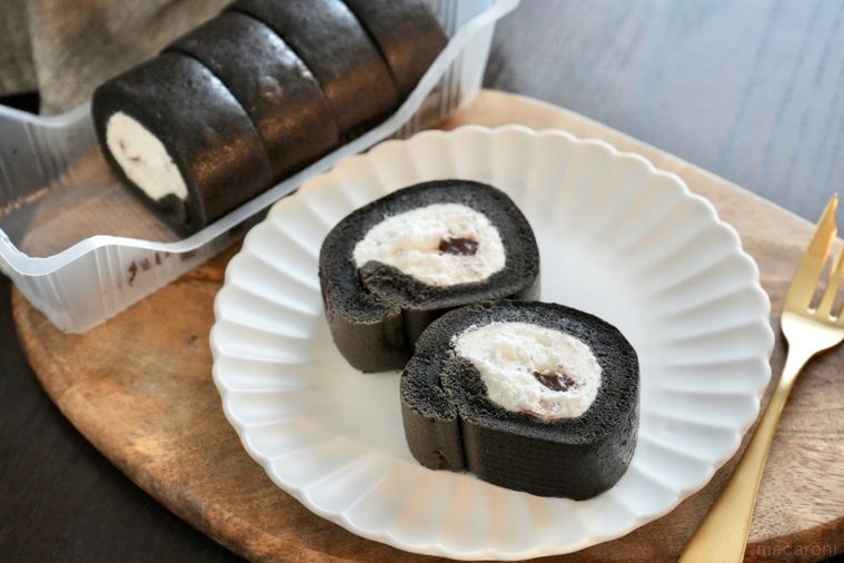 木のカッティングボードと白い皿にのったモノクロのロールケーキと金のフォーク