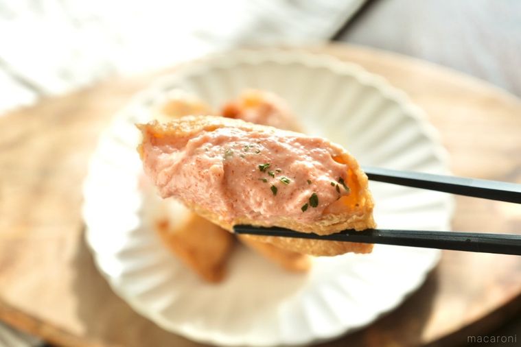 木のカッティングボードにのった白い皿と明太子マヨネーズソース和えがのった韓国風いなり寿司を黒い箸で持つ様子