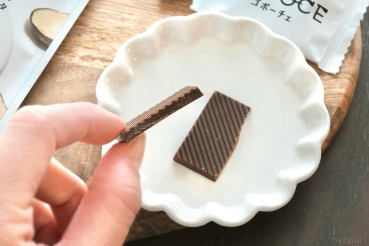 木のカッティングボードと白い小皿と手に持ったごぼう由来のチョコレート