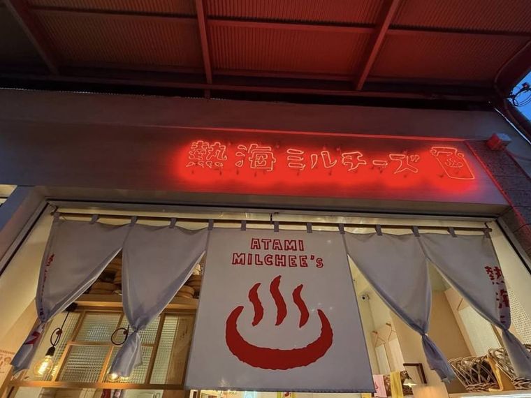 温泉マークの暖簾とネオンの看板がかかった熱海ミルチーズの外観