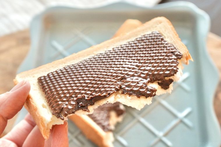 木のカッティングボードとブルーグレーの皿にのったトーストと生チョコスライスを手に持つ様子