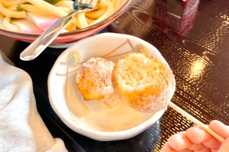 白い器から竹串でうどんドーナツを持ち上げる様子