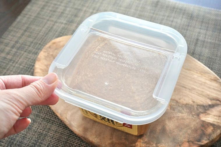 木のカッティングボードにのった味噌のプラスチックケースにフタを取り付ける様子
