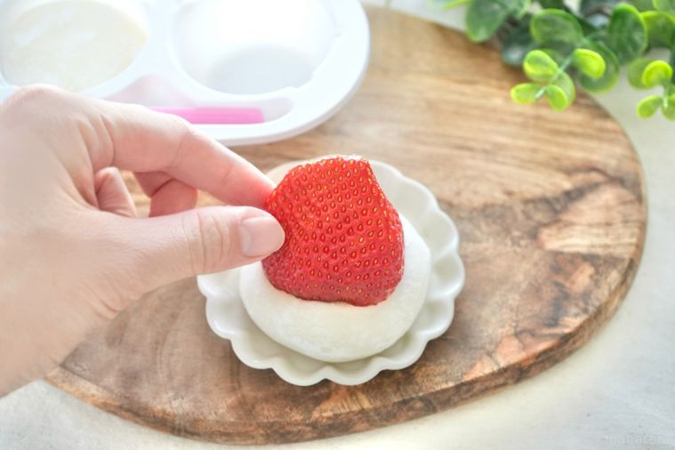 木のカッティングボードと白い小皿にのったいちごと生雪見だいふくとストライプの布とグリーン