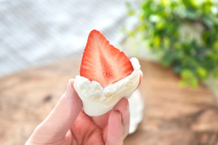 木のカッティングボードと白い小皿といちごのせ生雪見だいふくを手に持つ様子