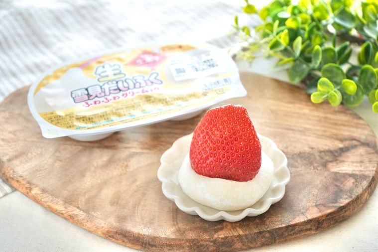 木のカッティングボードと白い小皿にのったいちごと生雪見だいふくとストライプの布とグリーン