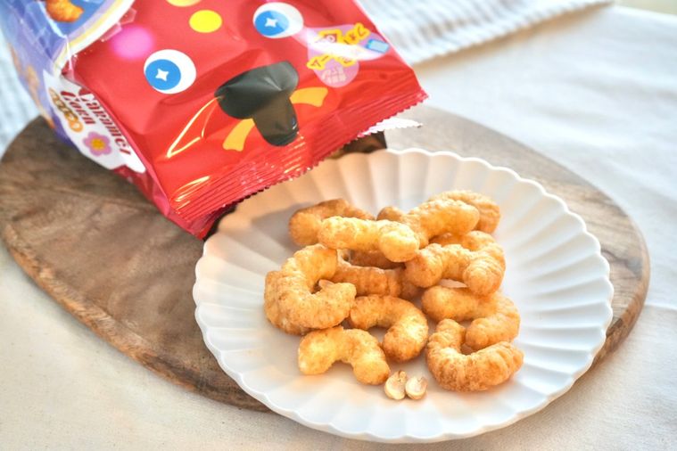 白いテーブルクロスと木のカッティングボードと白い皿にのったひなまつりパッケージのキャラメル味のコーンスナック