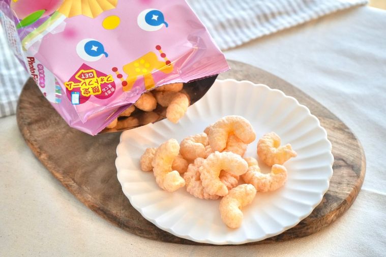 白いテーブルクロスと木のカッティングボードと白い皿にのったひなまつりパッケージの桃味のコーンスナック