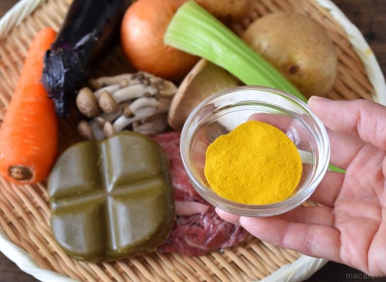 ざるに盛ったカレーの材料と手に持ったかぼちゃパウダー