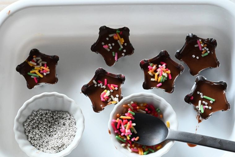 白いトレーの上でアルミカップにチョコレートを注ぎカラースプレーでトッピングする様子