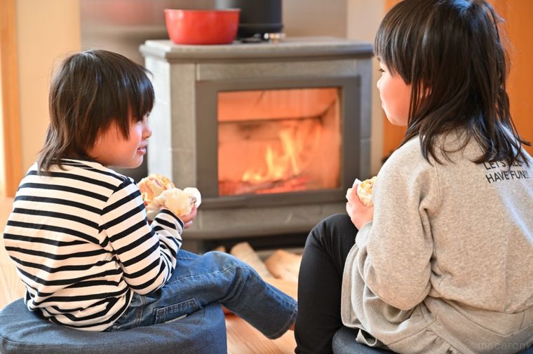 薪ストーブの前で2人の子どもがハンバーガーを食べている