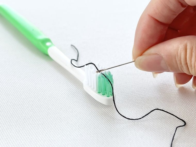 歯ブラシを使って針に糸を通そうとしている様子