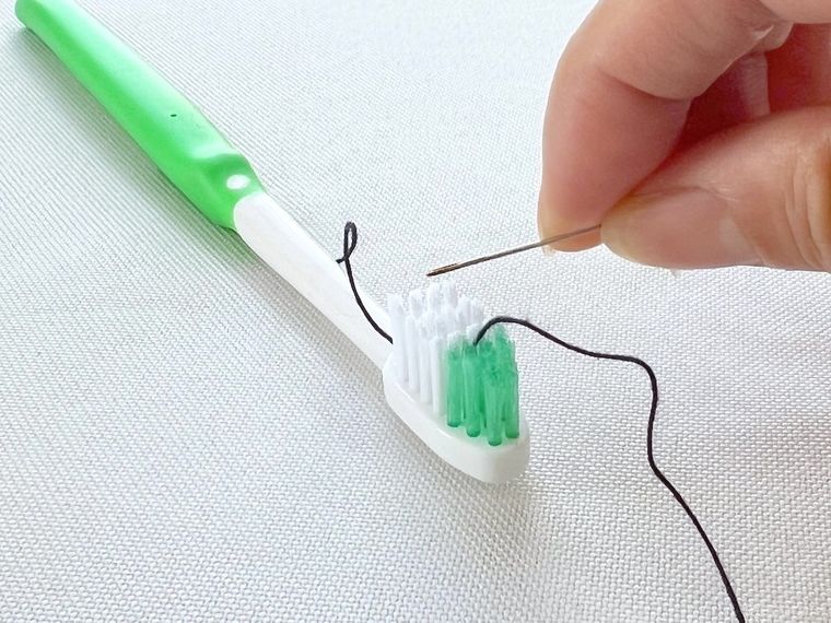 歯ブラシを使って針に糸を通そうとしている様子