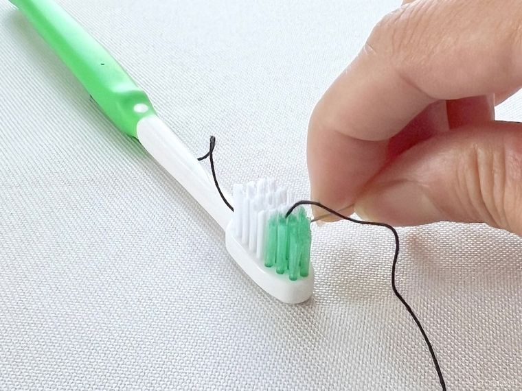 歯ブラシを使って針に糸を通そうとしている様子