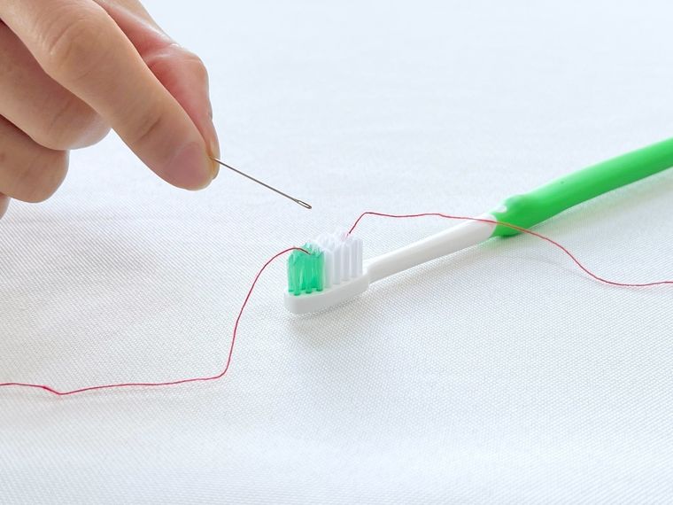歯ブラシを使って針に糸を通そうとしている様子