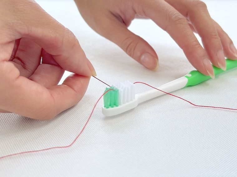 歯ブラシを使って針に糸を通そうとしている様子