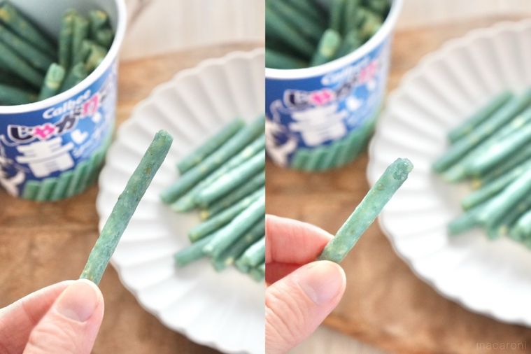 木のカッティングボードと白い皿にのった青いシーフードじゃがりことストライプの布と手