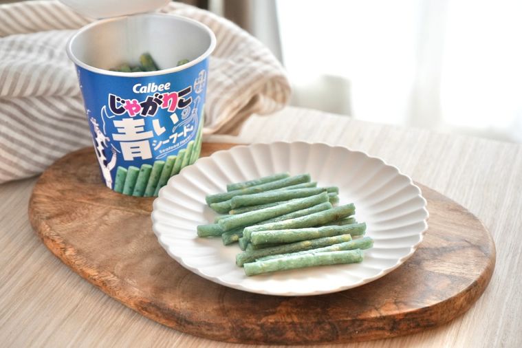 木のカッティングボードと白い皿にのった青いシーフードじゃがりことストライプの布