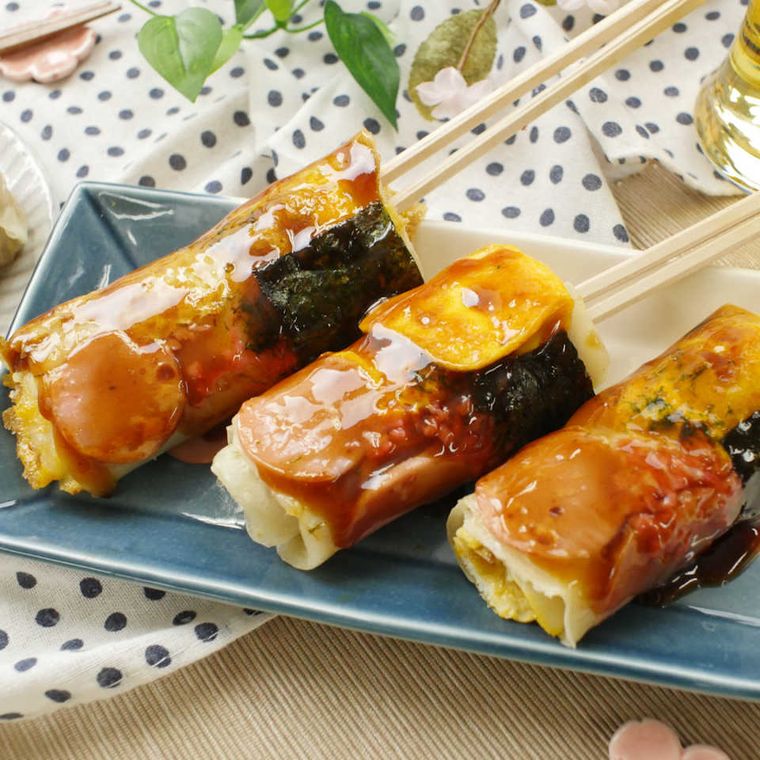 青い皿にのった串差しの魚肉ソーセージお好み焼き